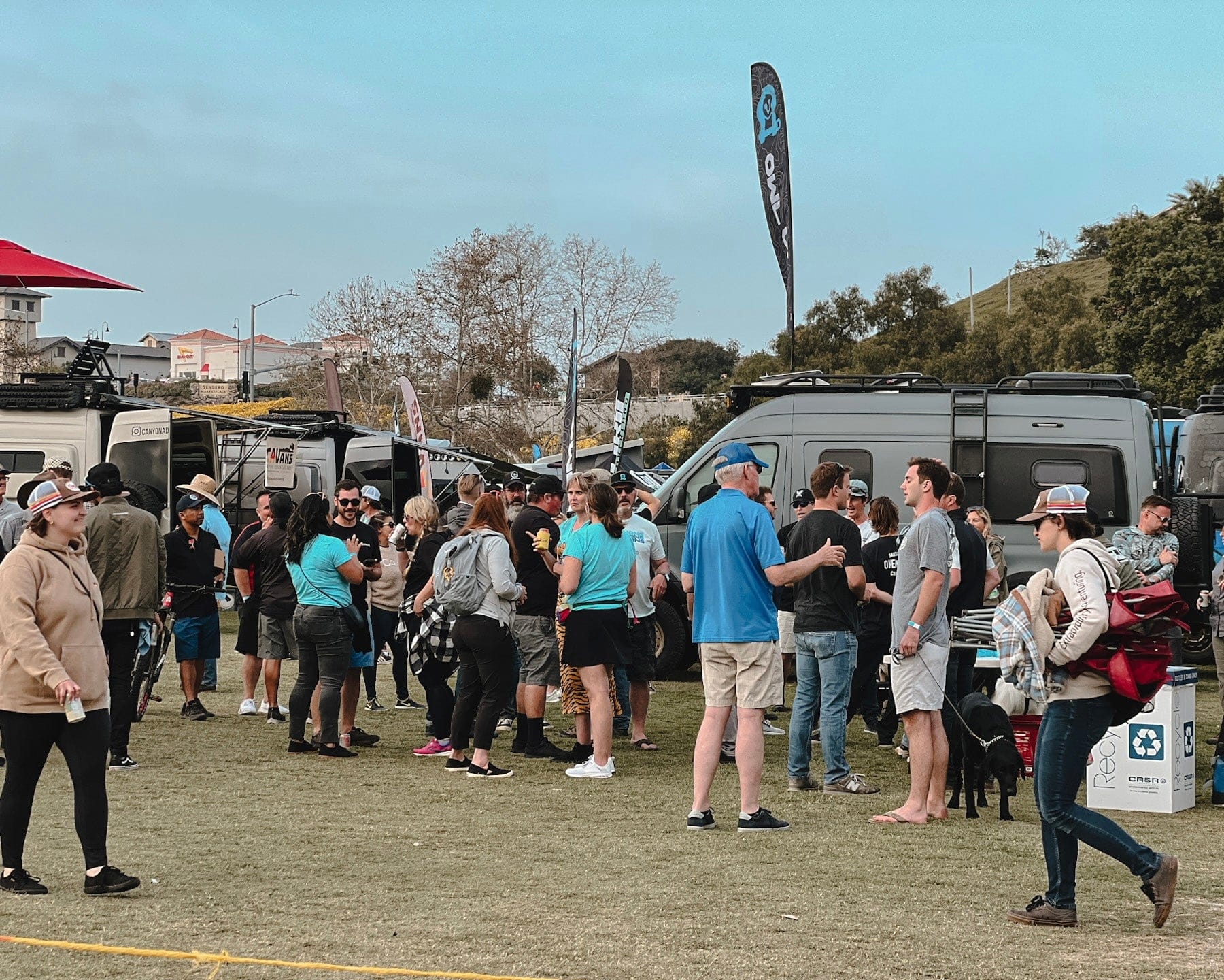 Vans, trucks, and outdoor gear on display between vendor booths at Backcountry Offroad Expo
