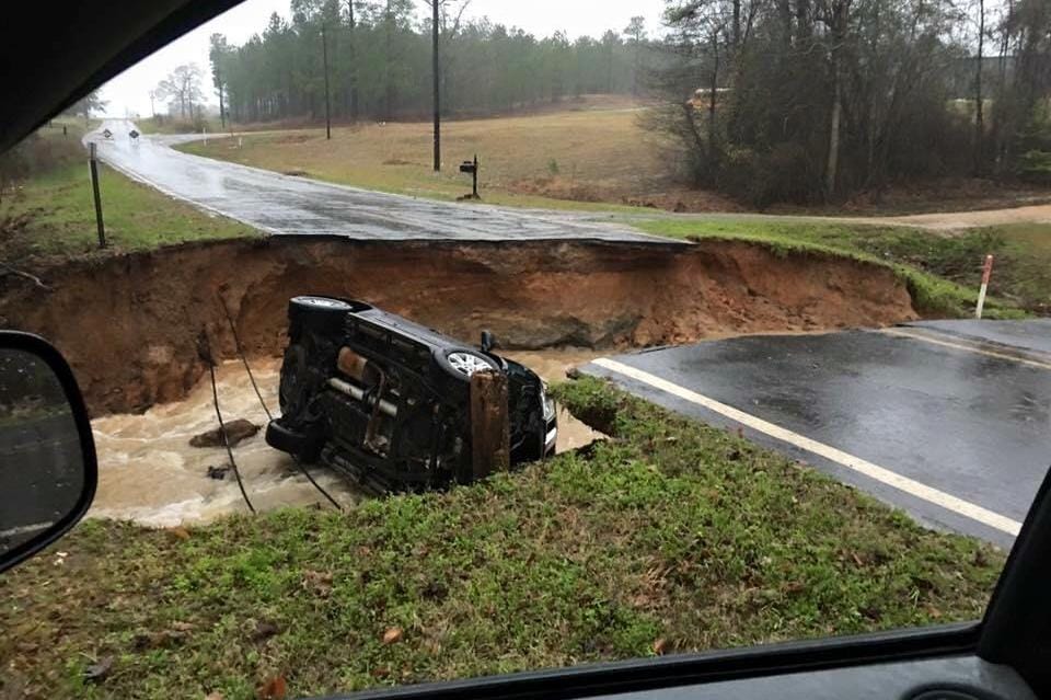 A washed-out road with a stranded vehicle after a Louisiana flood.