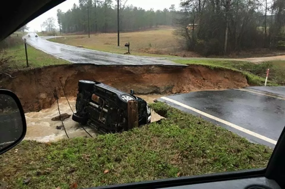 A washed-out road with a stranded vehicle after a Louisiana flood.