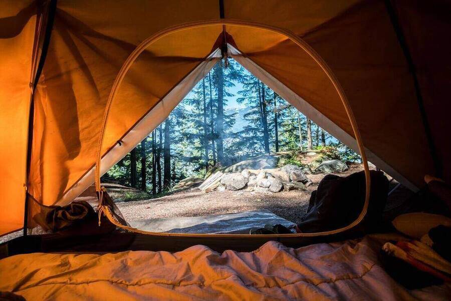 View from inside an orange backpacking tent looking out at a campfire ring in a Pacific Northwest pine forest at dusk.
