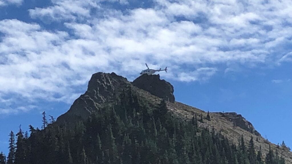 A rescue helicopter hovering above a Pacific Northwest alpine ridge during a backcountry extraction.