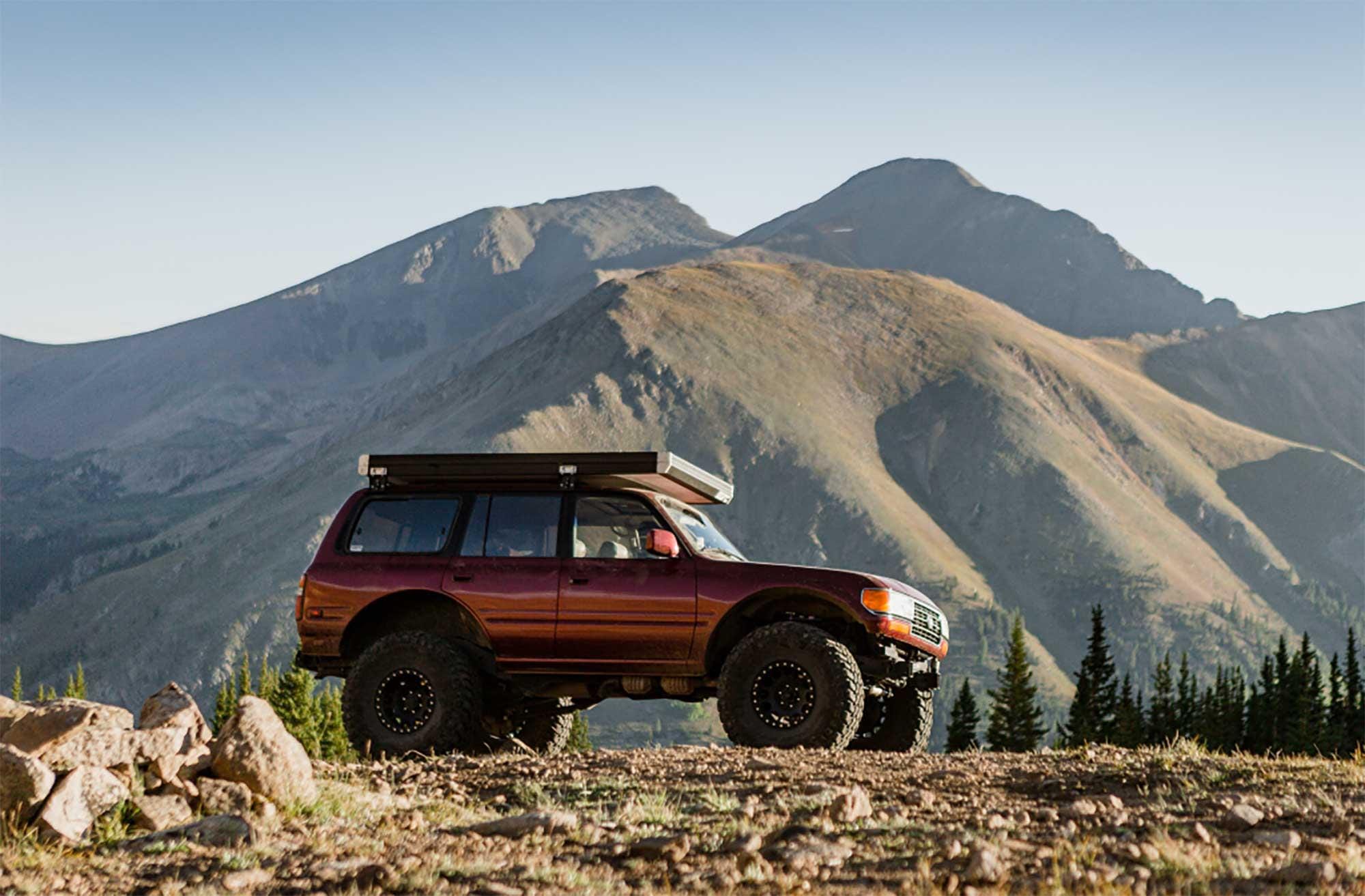 A maroon Toyota Land Cruiser on a Forest Service 5000 road with mountain peaks in the background