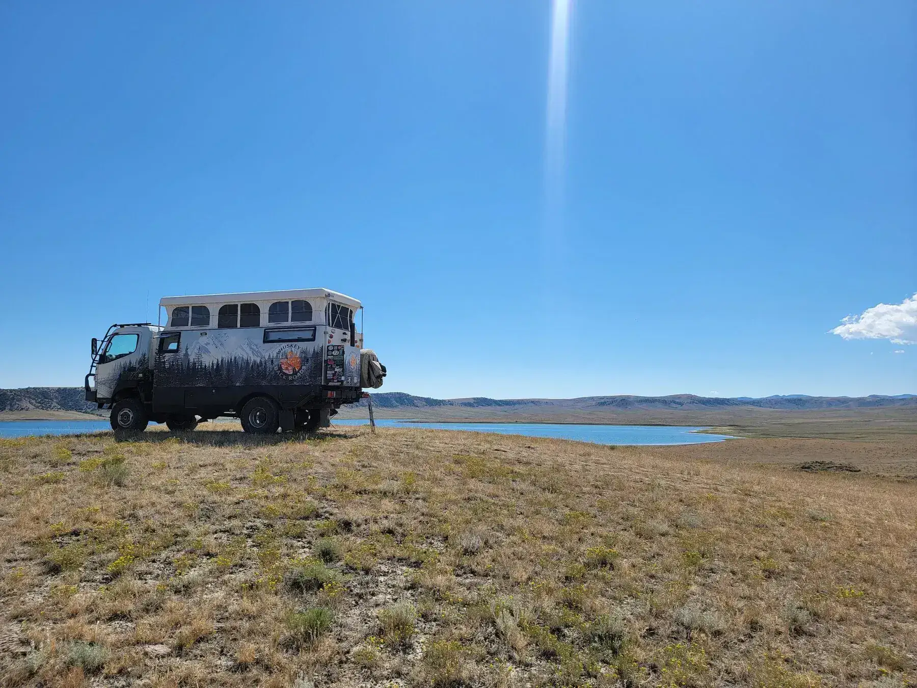 Off-road camper truck beside a blue lake