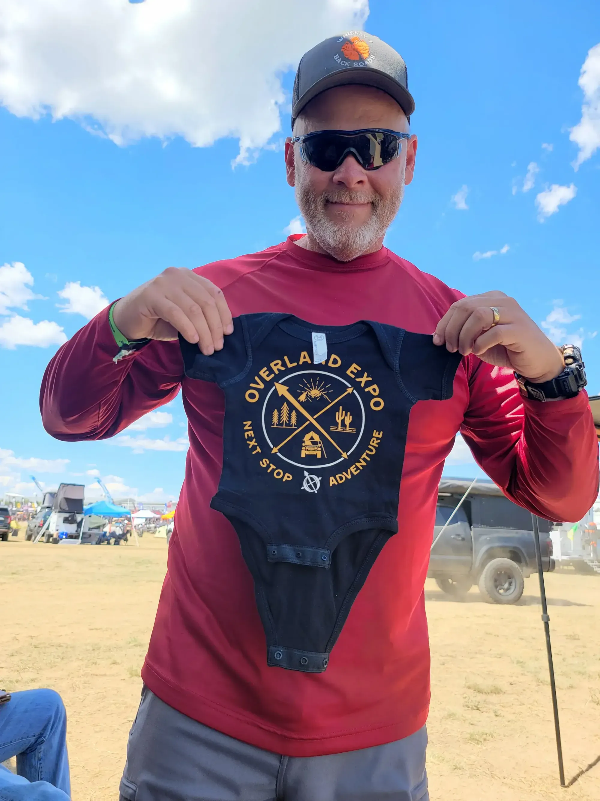 Man holding an adventure-themed baby onesie outdoors