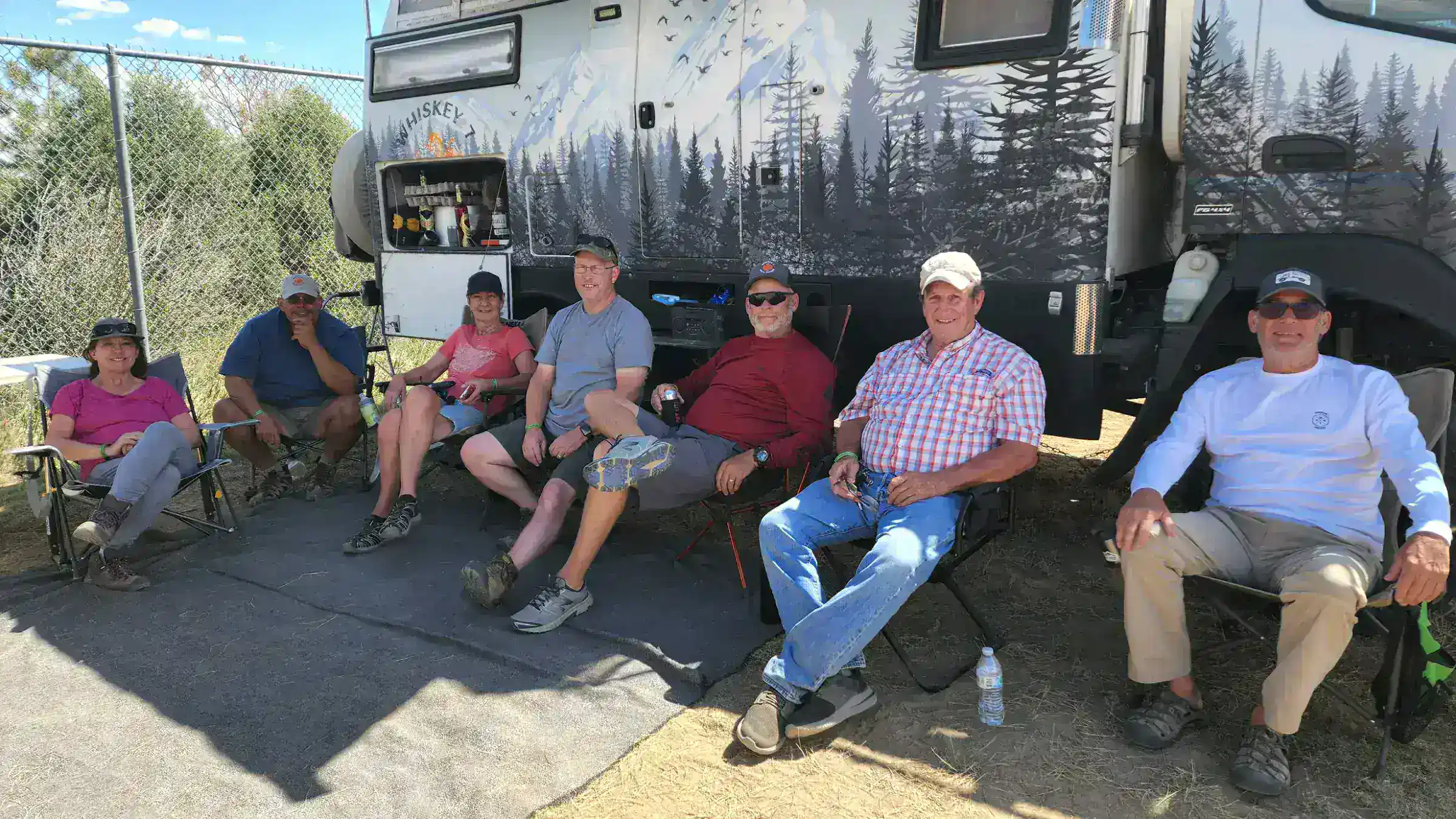Six adults beside a mountain-themed recreational vehicle