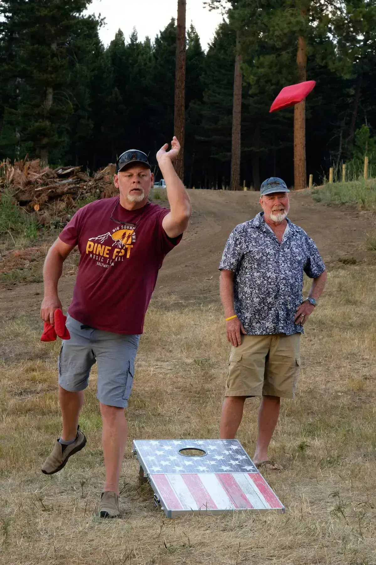 Two men playing cornhole in a forest clearing