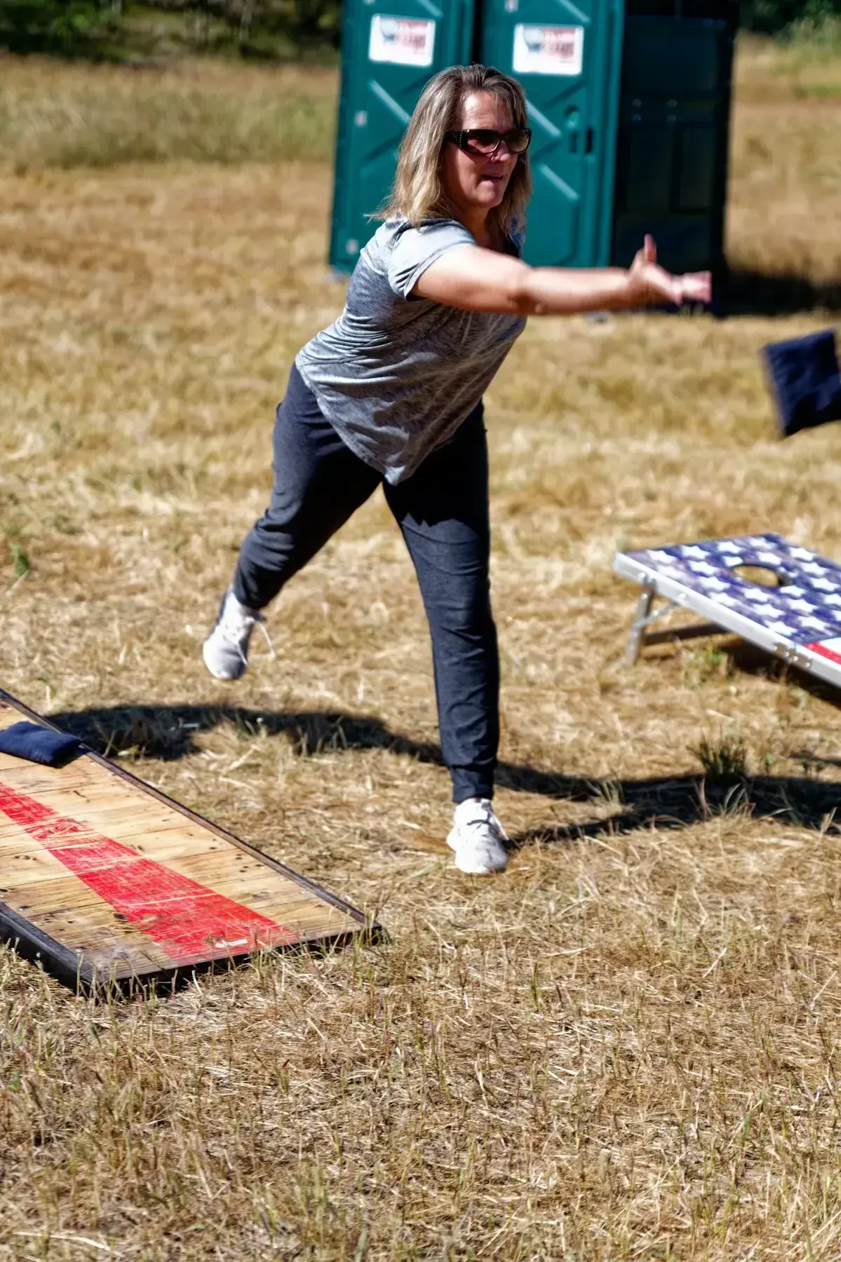 Woman beside a cornhole board in a grassy field