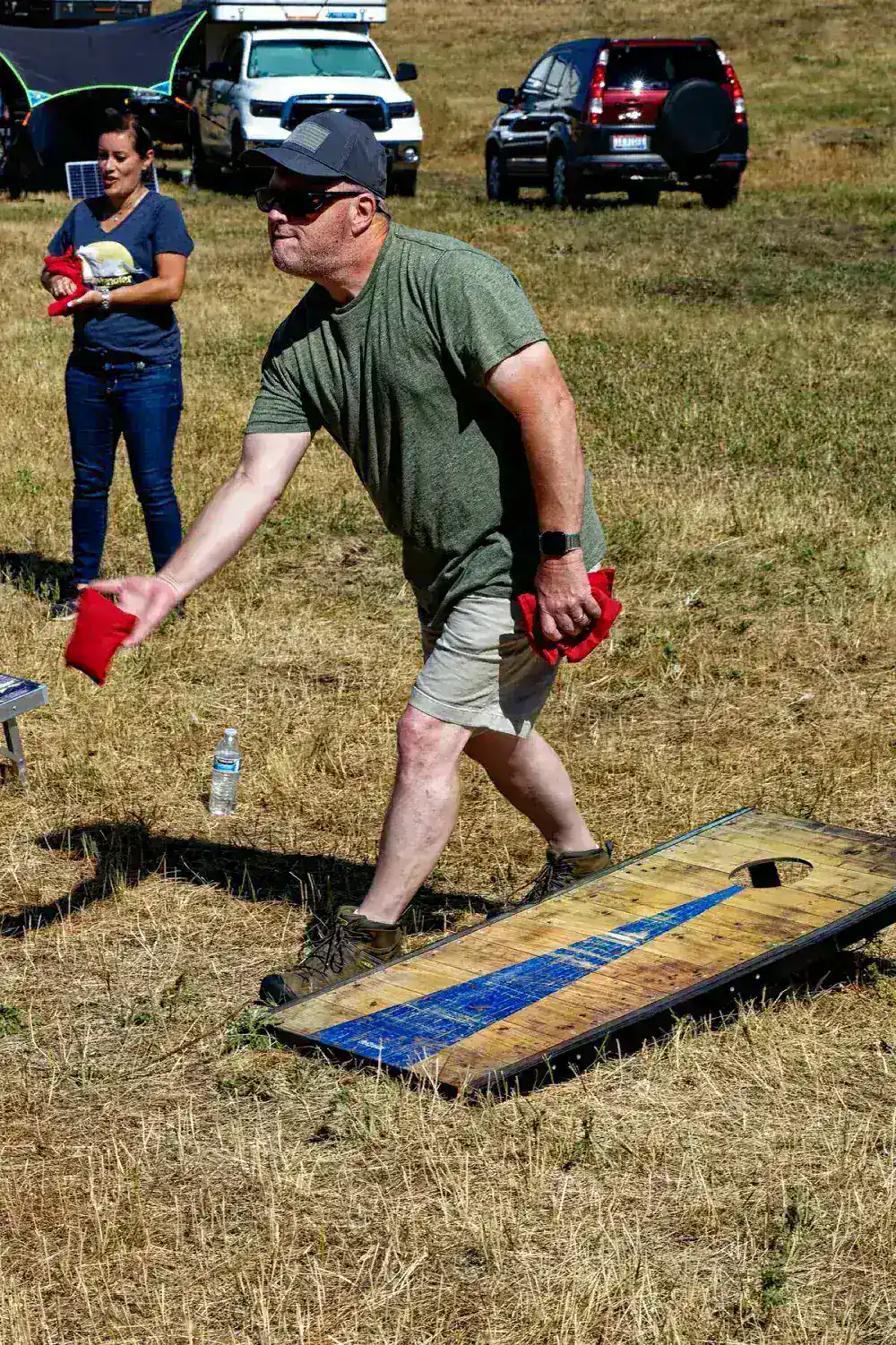 Man tossing a red beanbag toward a cornhole board