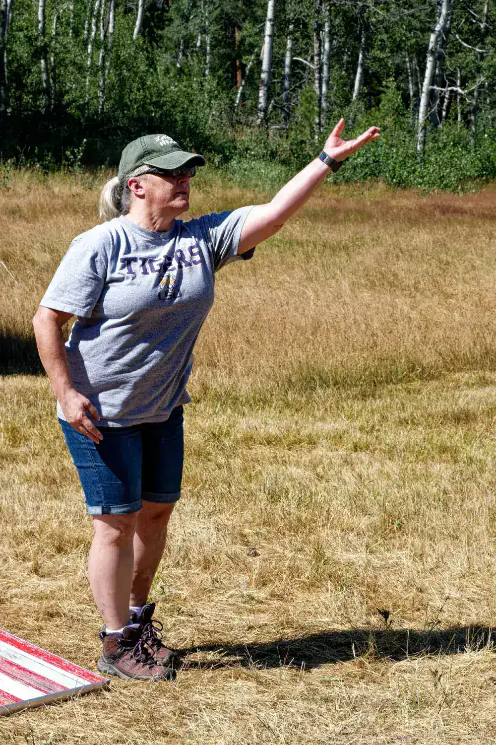 Woman in a Tigers shirt gesturing beside a birch forest