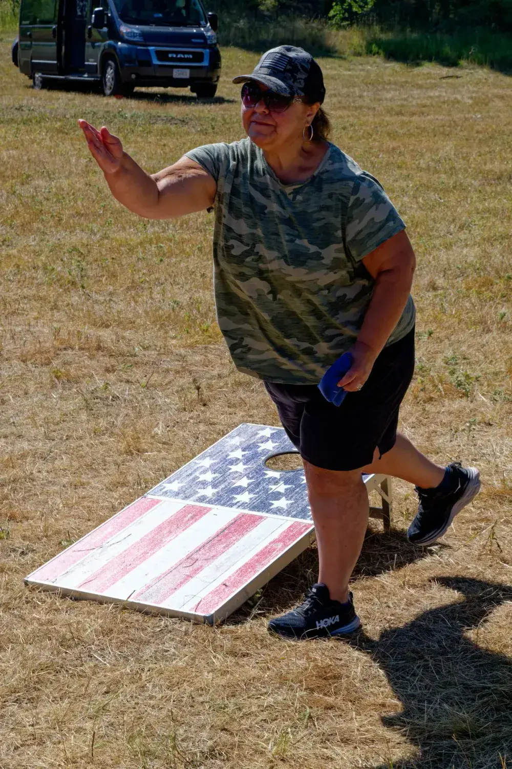 Woman holding a beanbag beside an American flag cornhole board