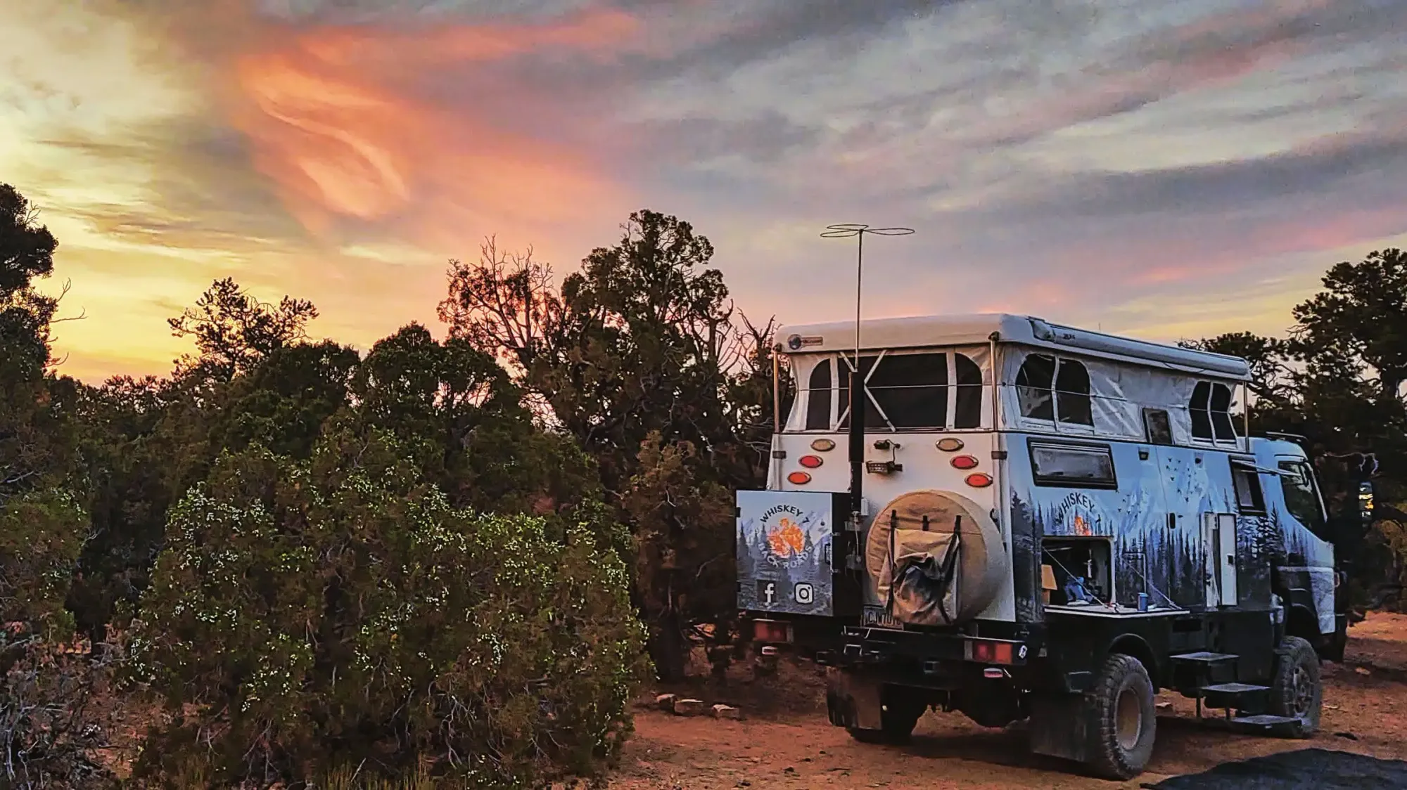 White expedition truck beside shrubs at sunset