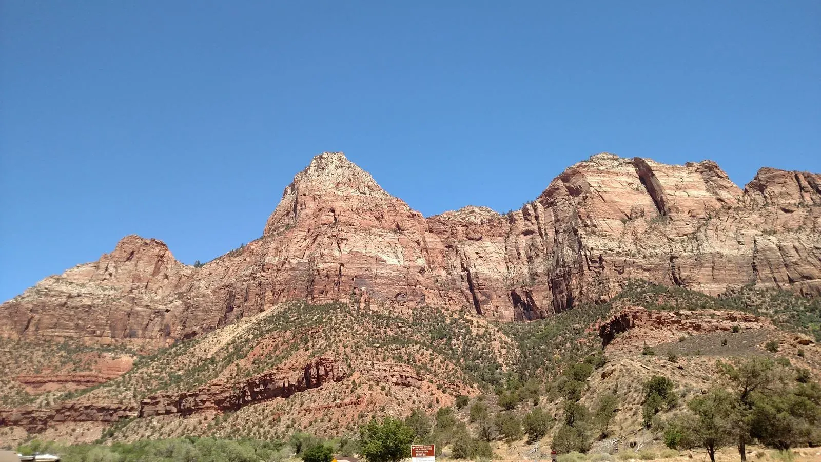 Red rock cliffs and peak with a Zion National Park sign
