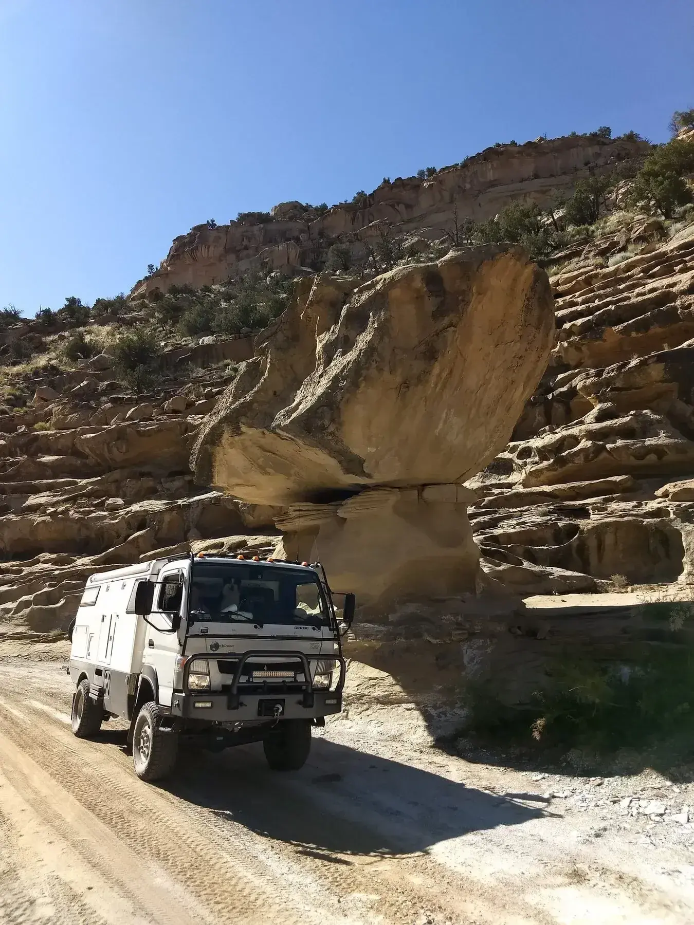 White expedition truck beneath a balanced sandstone boulder