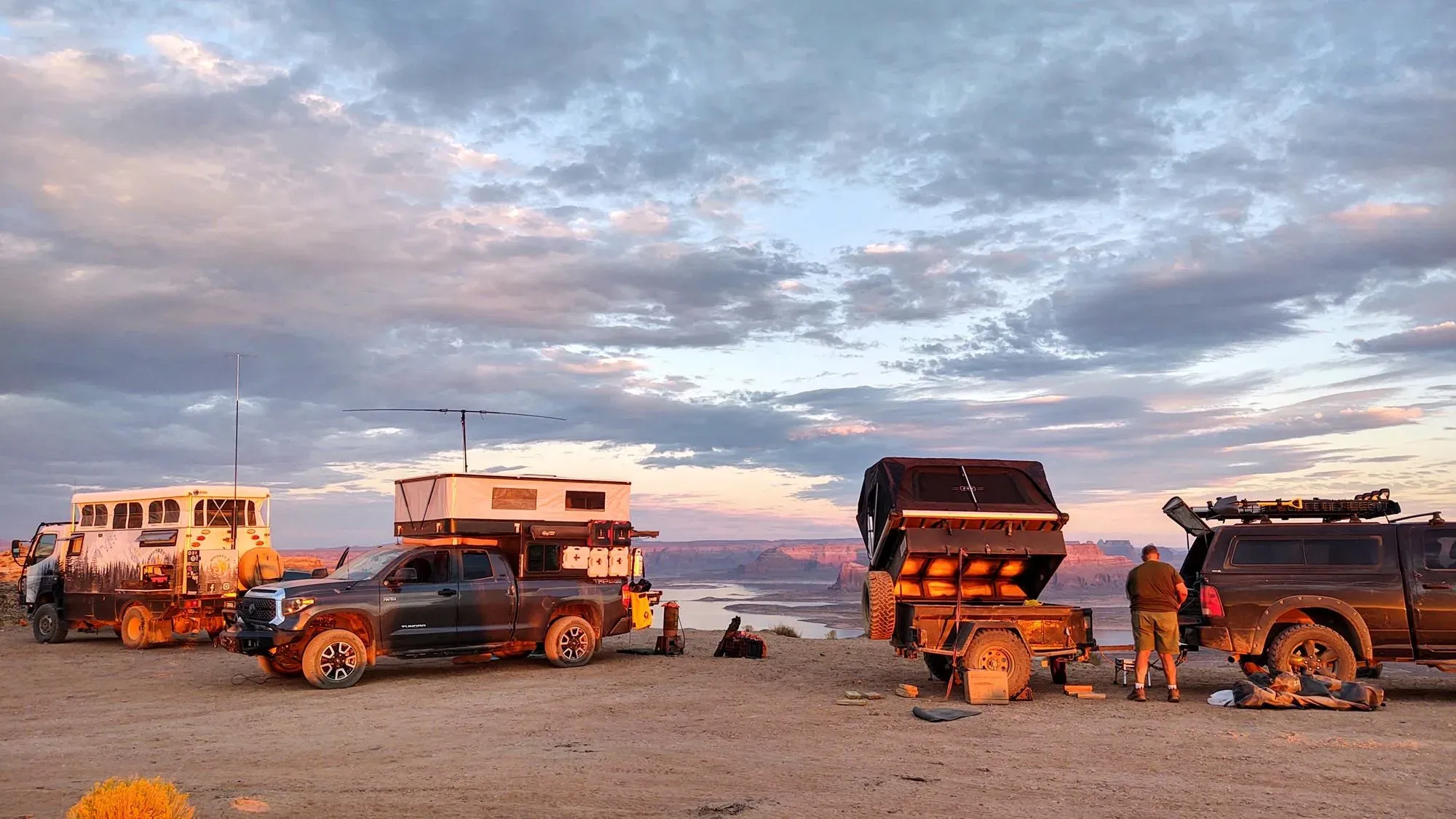Off-road vehicles and trailers above a canyon at sunset