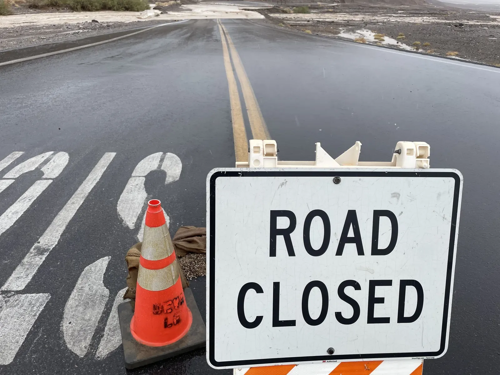 Road Closed sign and orange cone on Badwater Road with floodwater beyond