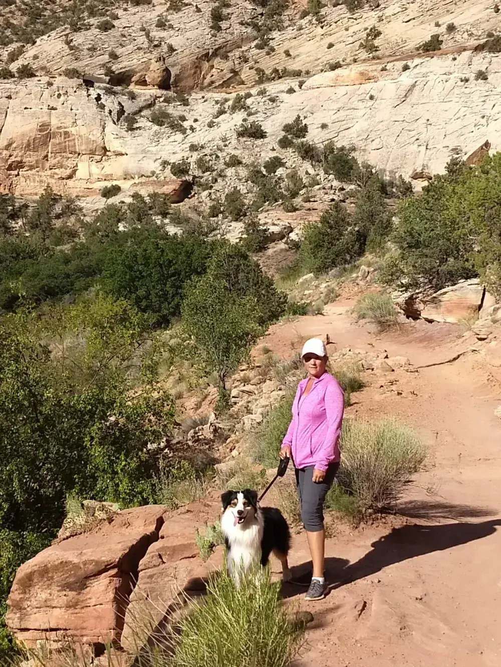 Woman and dog on a rocky desert trail beneath sandstone cliffs
