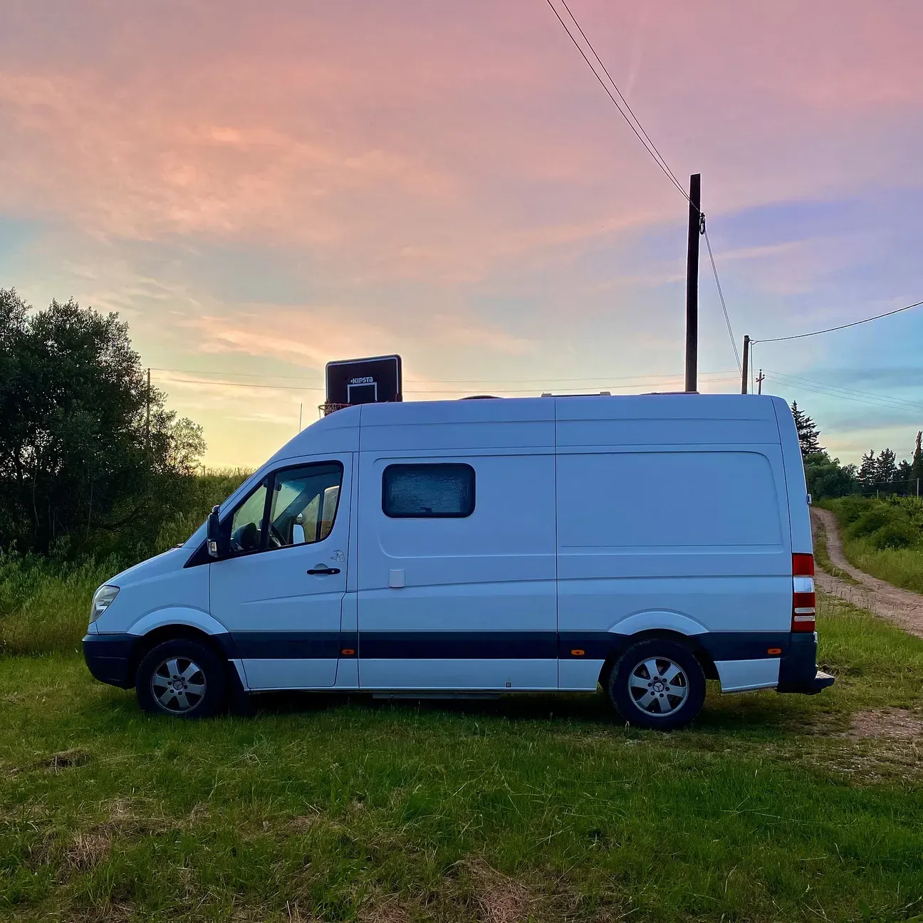 Converted Mercedes Sprinter van parked alone in a grassy field at dusk.