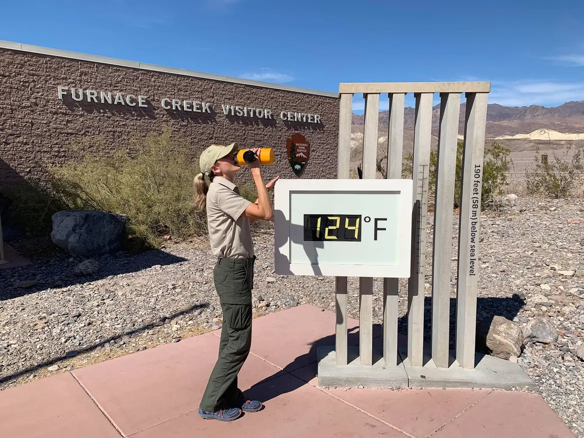 Volunteer drinking water beside an outdoor thermometer in Death Valley