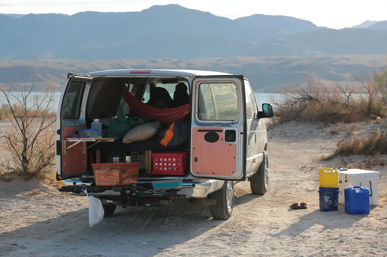 Ford E350 camper van conversion with rear doors open parked on the gravel shore of Lake Mead.