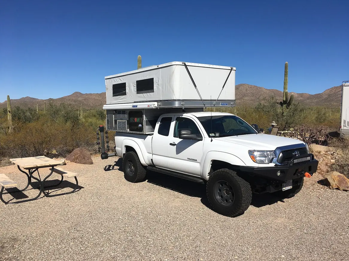White Four Wheel Camper pop-up slide-in camper on a white Toyota Tacoma at a desert campsite with saguaro cactus.