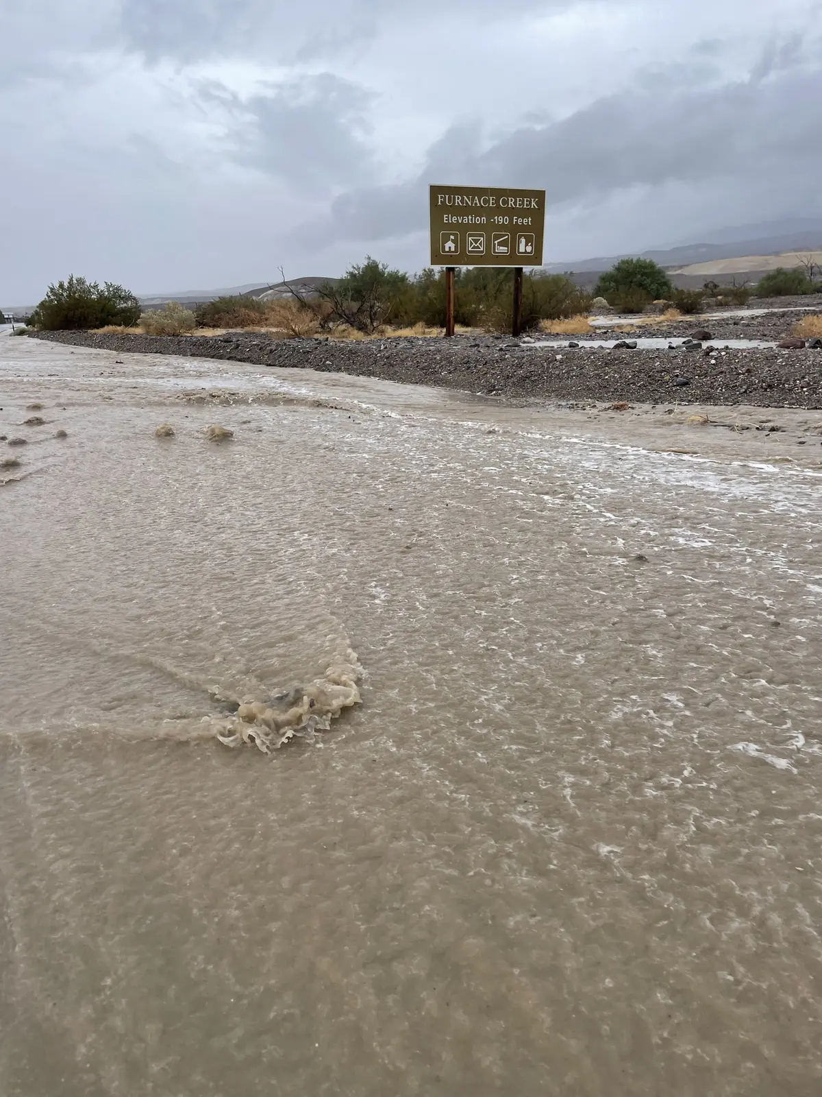 Muddy floodwater covering CA 190 near a Furnace Creek road sign