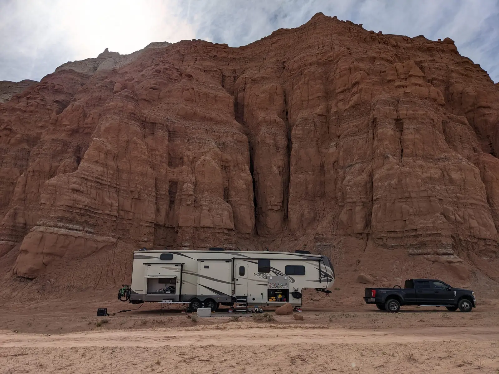 Black pickup truck and large white fifth-wheel trailer parked below red rock cliffs at Goblin Valley State Park, Utah.