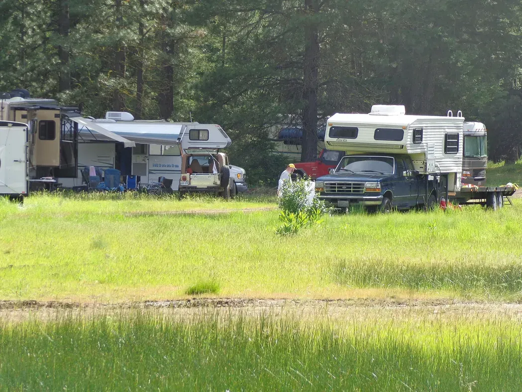 A slide-in truck camper on a pickup and a Class C motorhome parked at BLM Liberty Recreation Site in the Oregon forest.