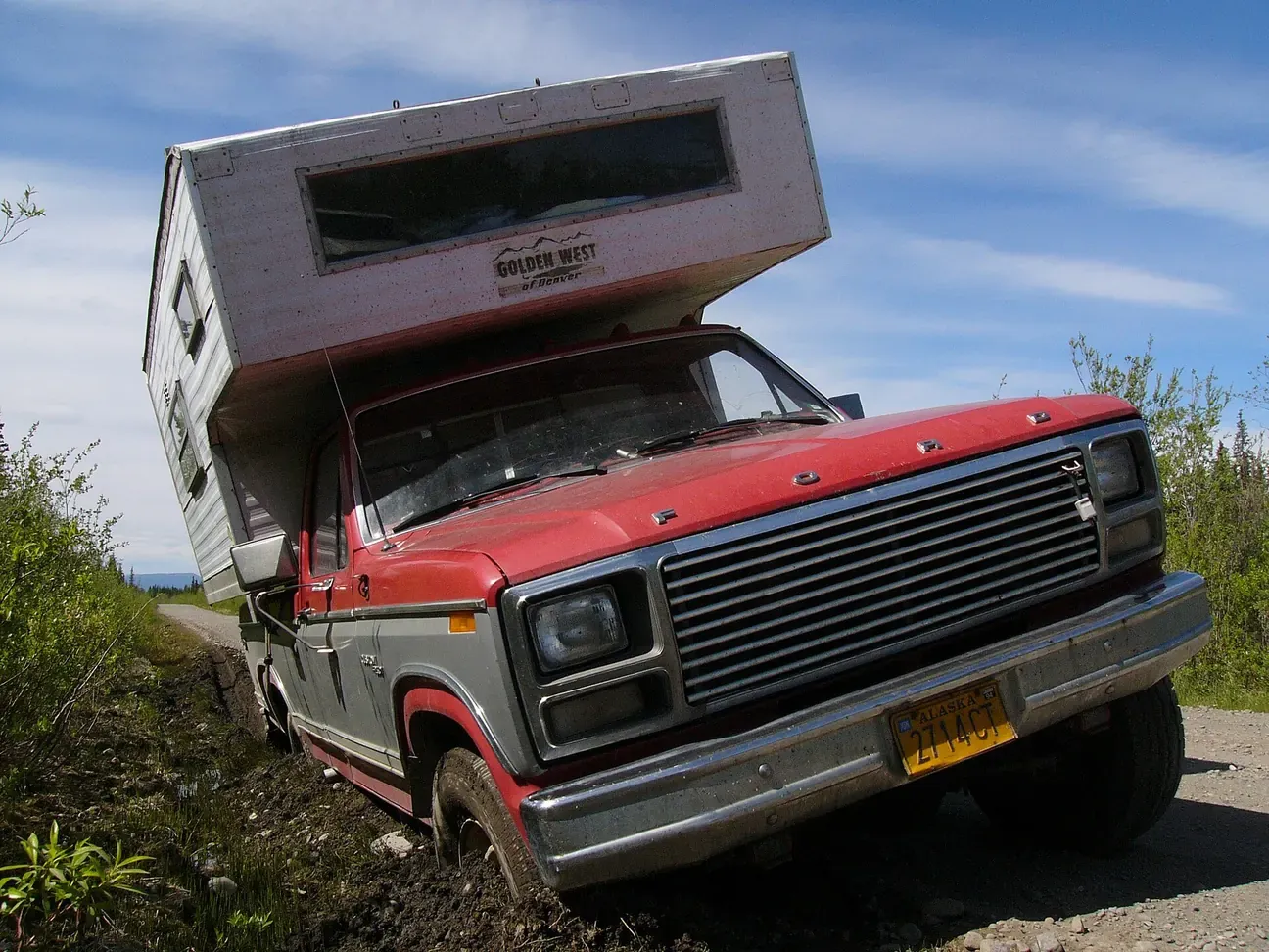 Pickup truck with a slide-in camper stuck on a gravel road in Alaska.