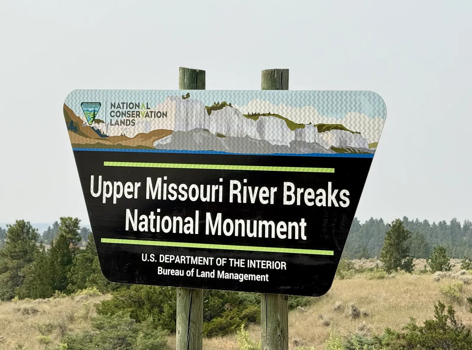 The Upper Missouri River Breaks National Monument entrance sign from the Bureau of Land Management, with pines and dry grass behind it
