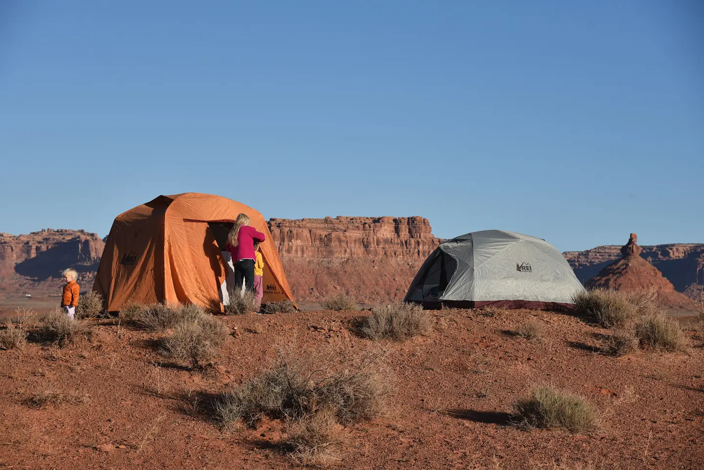 A family emerges from a large orange tent in the desert landscape of Valley of the Gods, Utah