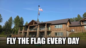 YouTube-style thumbnail: two-story mountain lodge home with American flag on a flagpole in front, with white text FLY THE FLAG EVERY DAY at the bottom.