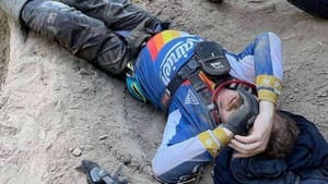An injured Pacific Northwest dirt bike rider lying on the ground after an inReach SOS incident, holding his helmet.